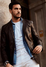 Load image into Gallery viewer, Man wearing a leather jacket over a denim shirt and white pants, standing against a neutral wall.