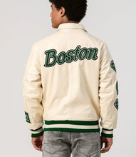 Load image into Gallery viewer, Person wearing a cream varsity jacket with &#39;Boston&#39; printed on the back, standing against a light gray background.
